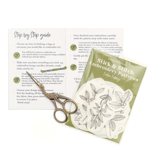 A pair of brass Stork scissors on top of an open instruction card and pack of embroidery pattern stickers