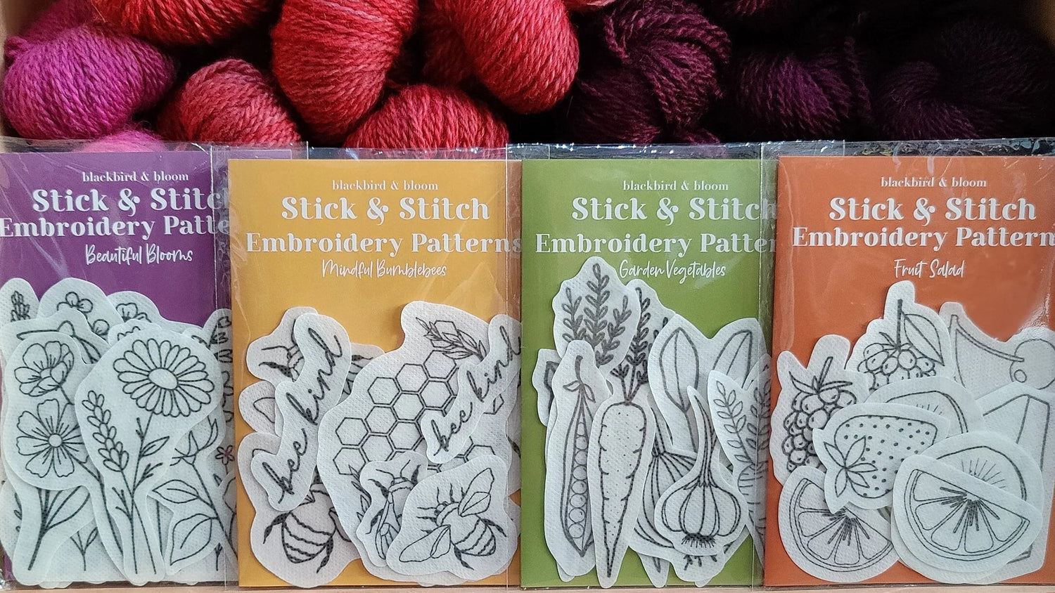 Yarn skeins with 'Stick & Stitch' embroidery pattern books on a wooden shelf.