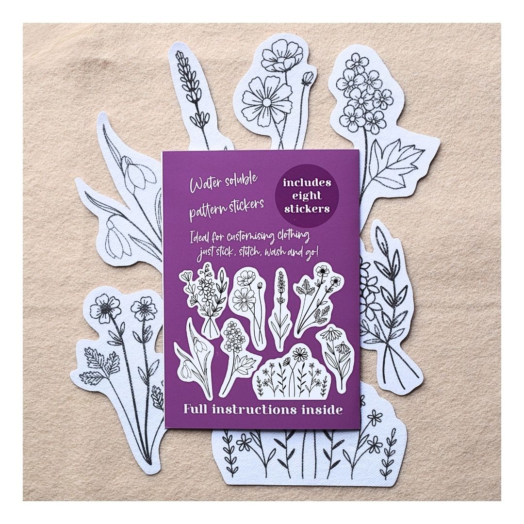 Water soluble pattern stickers featuring botanical and floral designs, shown with a purple packaging card on a textured beige background.